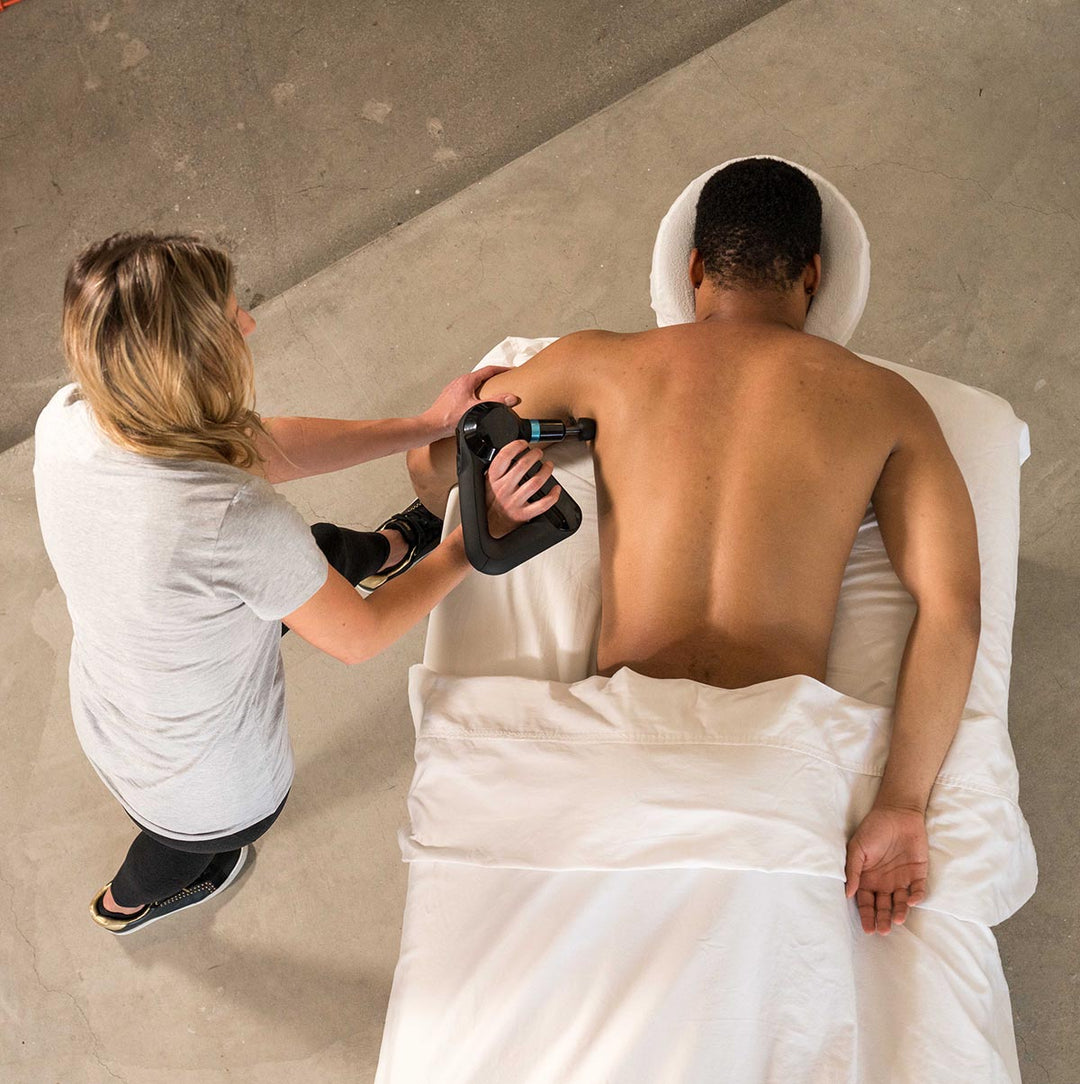 Therapist using a Theragun on a client's upper back and shoulders