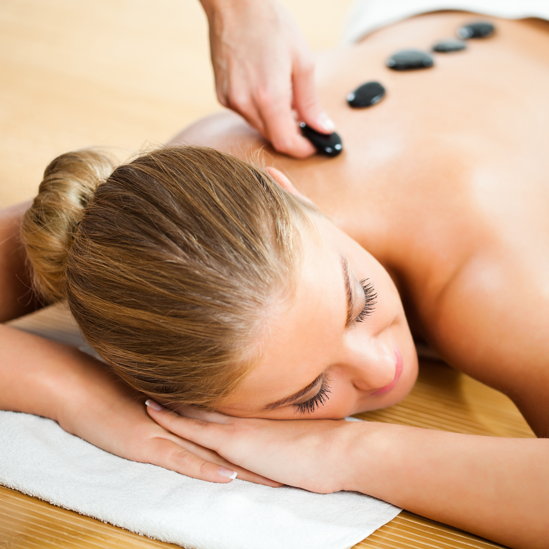 Woman relaxing face down as warm stones are placed along her back during a hot stone massage