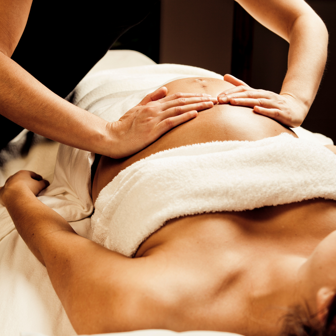Therapist's hands resting gently on a bump during a pregnancy massage