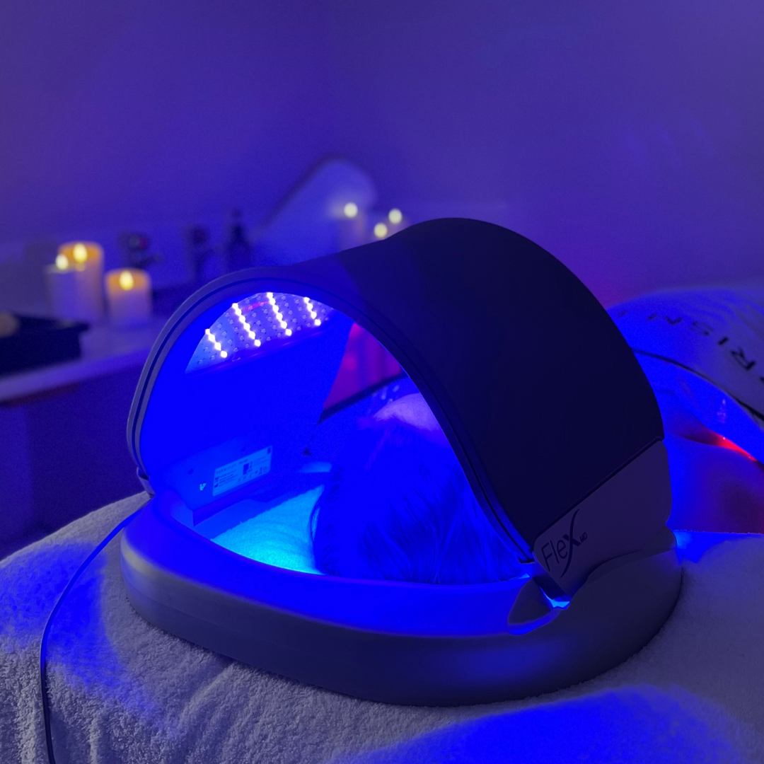 Dermalux LED canopy glowing blue over a treatment bed in a candlelit room