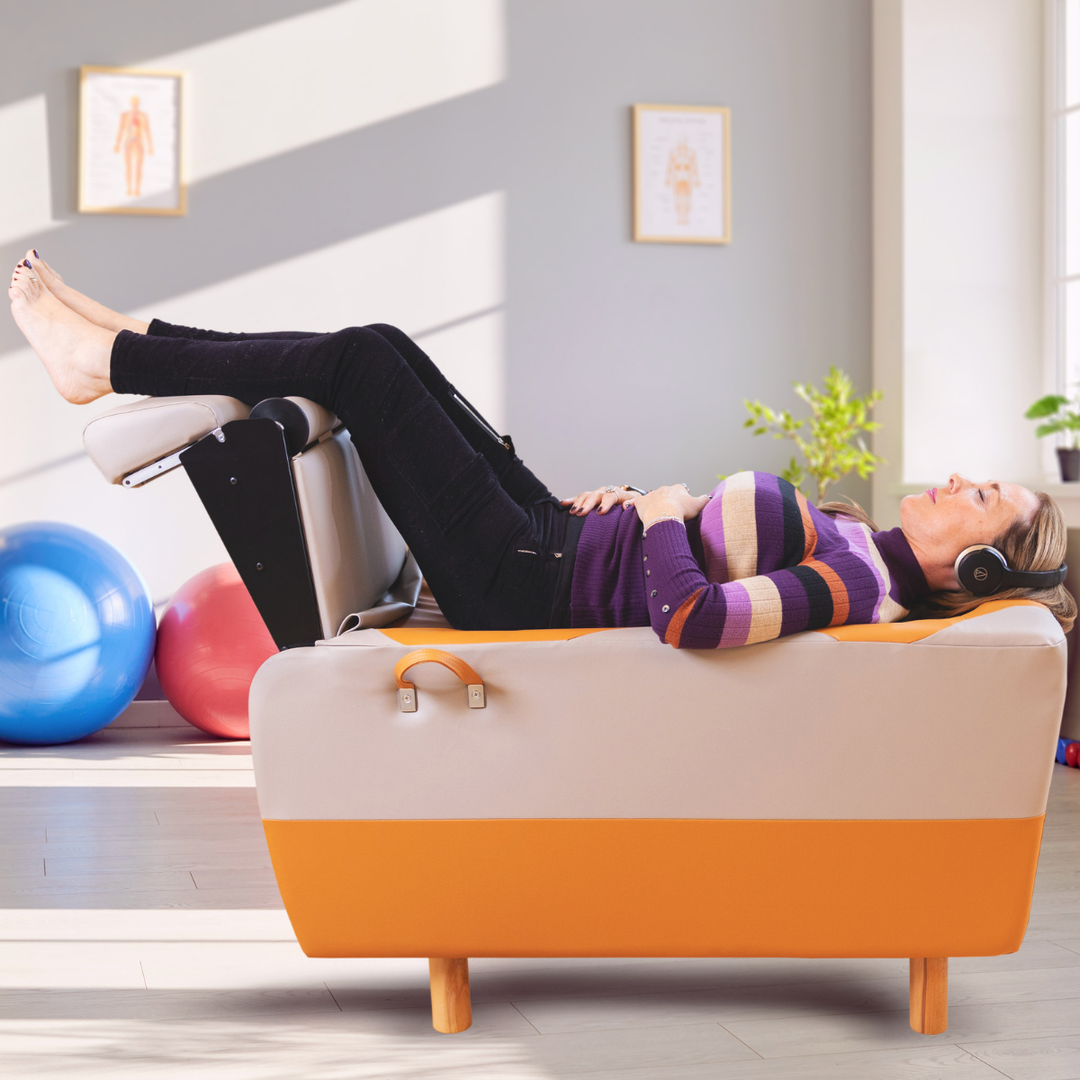 Person lying fully clothed on a BackHug robotic back therapy bed with legs raised, wearing headphones